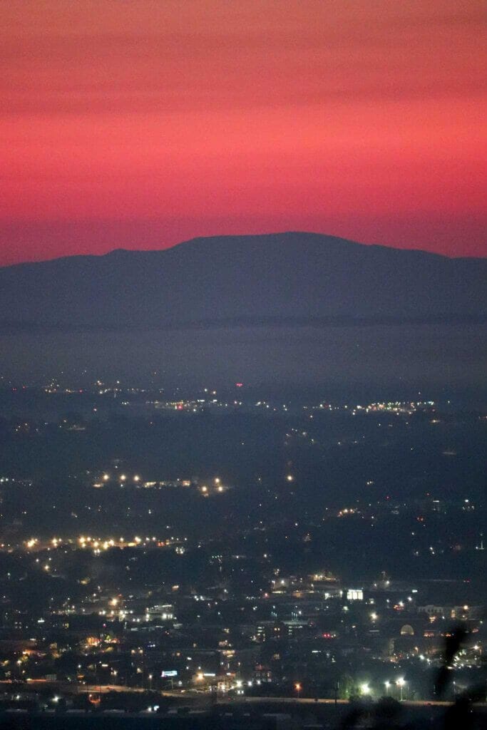 red sunrise sky behind a mountain as the chattanooga lights twinkle in the valley below